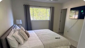 Une chambre à coucher avec un lit, une table de chevet avec une lampe, une fenêtre avec des rideaux et un téléviseur fixé au mur.