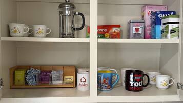 A kitchen with white shelves containing various items like a coffee maker, tea boxes, and mugs.