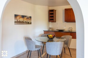 A dining area with a glass table, four grey chairs, a bowl of fruit, and a cityscape painting on the wall. - Villa AGUILA by Abahana Villas (Benitachell)