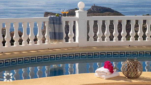 A poolside view with a white balustrade, a towel, a decorative vase, and a bottle of orange juice. - Villa AGUILA by Abahana Villas (Benitachell)