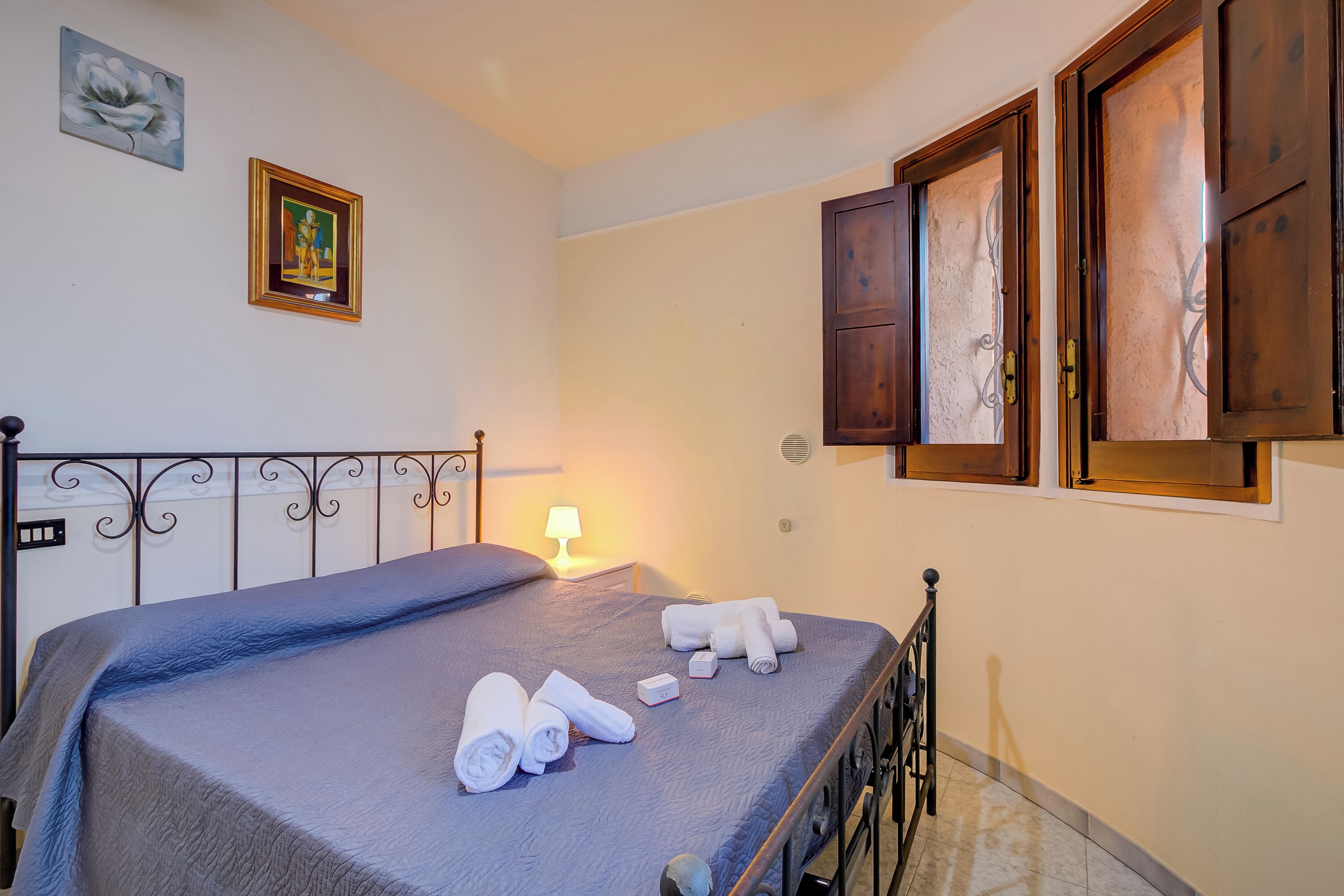 A neatly made bed with rolled towels, a bedside lamp, and a wall-mounted artwork.