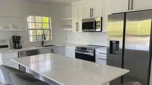 Een moderne keuken met witte kasten, een roestvrijstalen koelkast, een inbouwoven en een groot eiland met barkrukken.