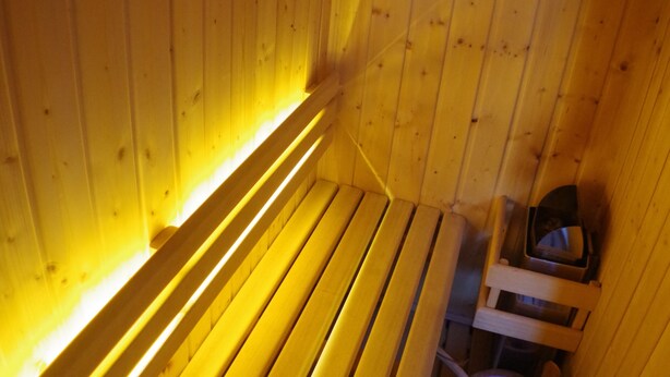Un sauna avec des bancs en bois et une petite table en bois, accompagnée d’un seau.