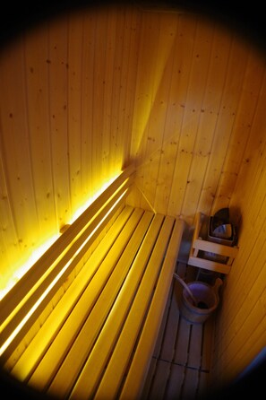 Een sauna met houten banken en een klein houten tafeltje met een emmer.