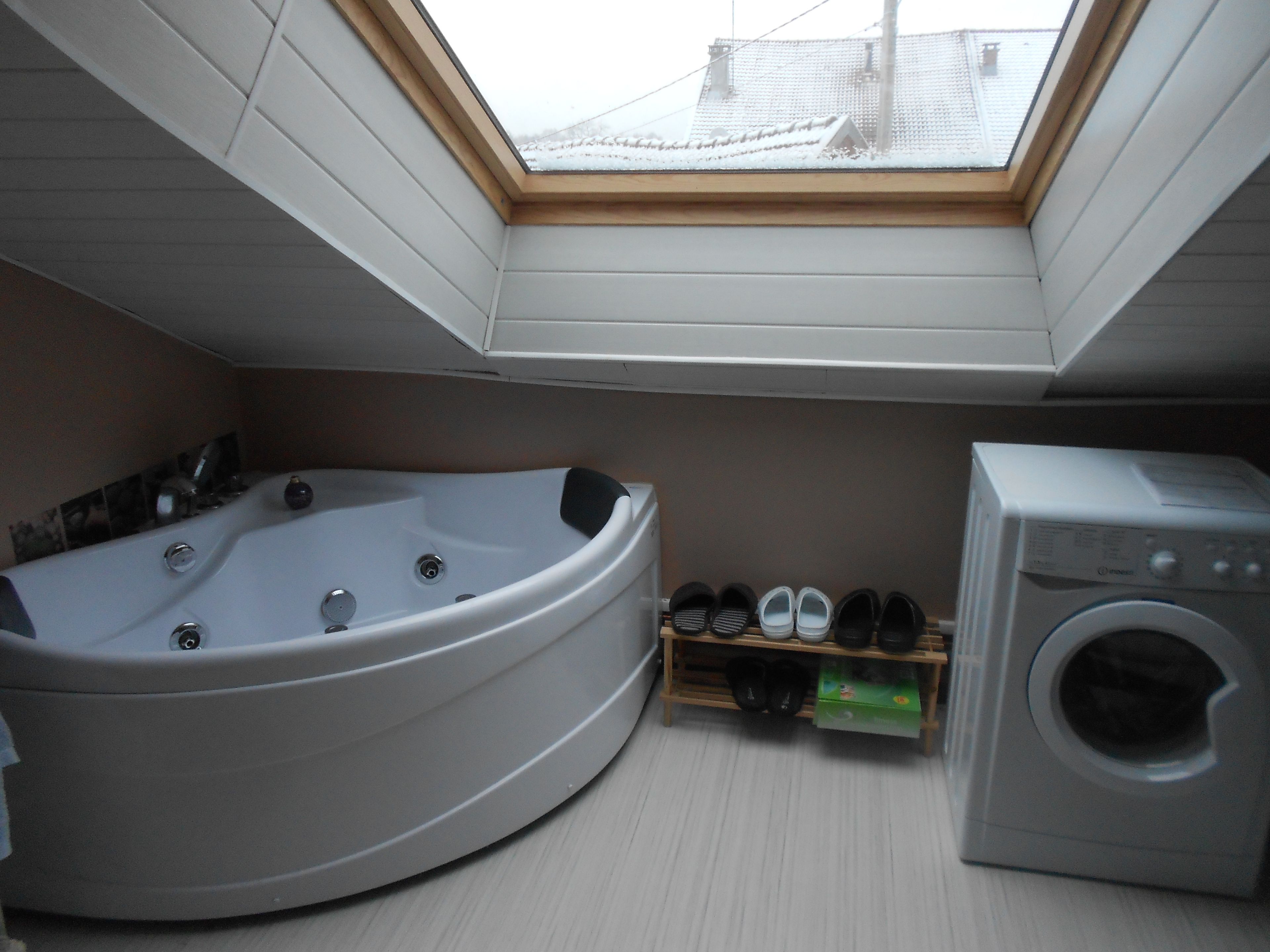 Ein Zimmer mit Dachfenster, einer Badewanne, einer Waschmaschine und einem Schuhregal.