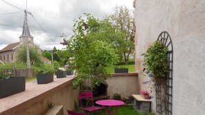 Un petit patio extérieur avec une table et des chaises, un mur en briques et un espace jardin agrémenté de plantes et d’un arbre.
