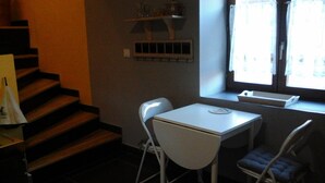 Une petite cuisine avec une table et des chaises blanches, une fenêtre avec des rideaux et un escalier.