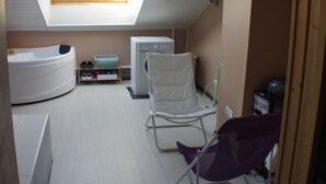 Une pièce de taille modeste, dotée d’une lucarne, d’un lave-linge, d’une chaise et d’une baignoire.