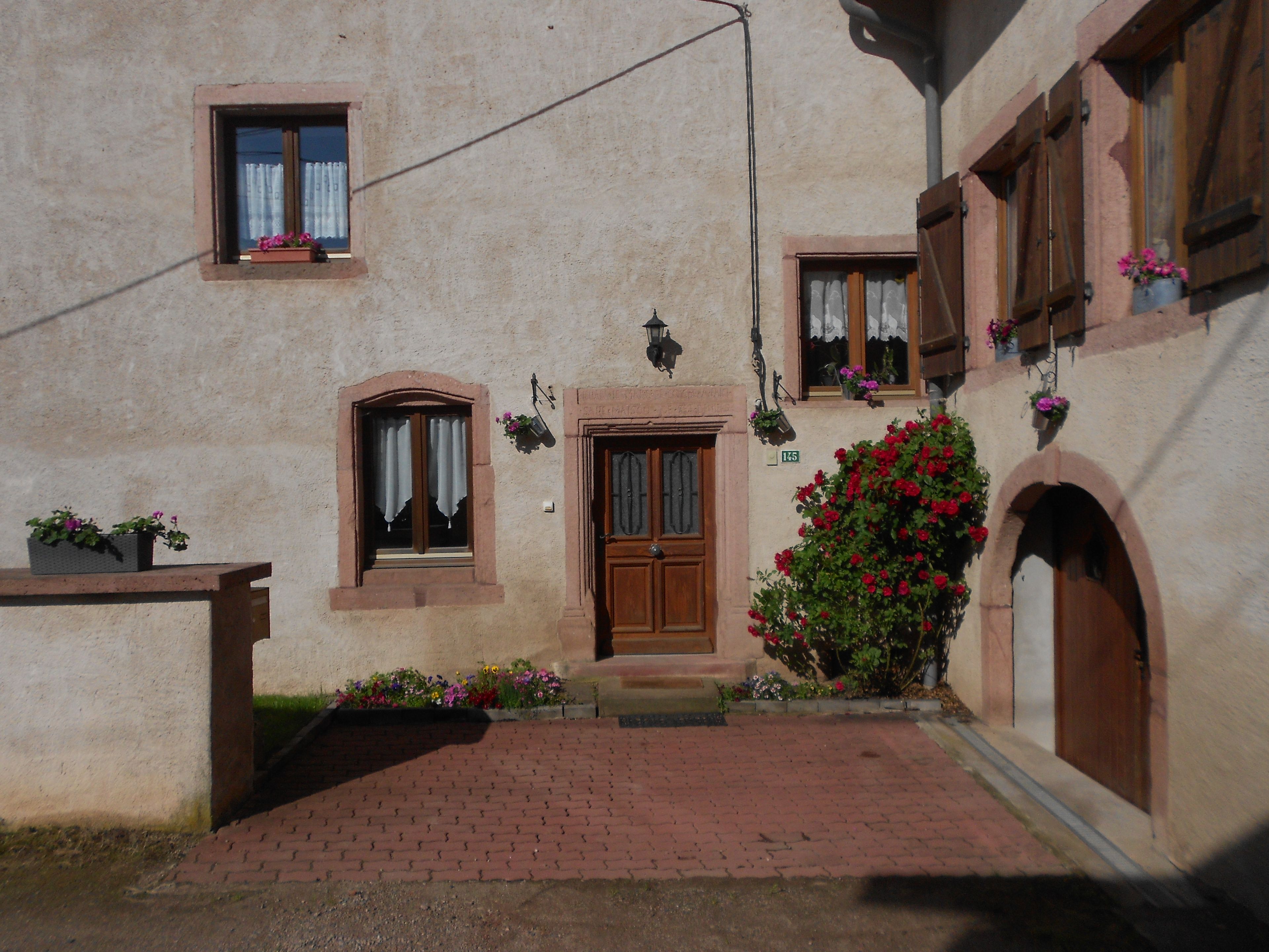 A building with a central entrance, a small window with a flower box, and a brick pathway leading to the entrance.