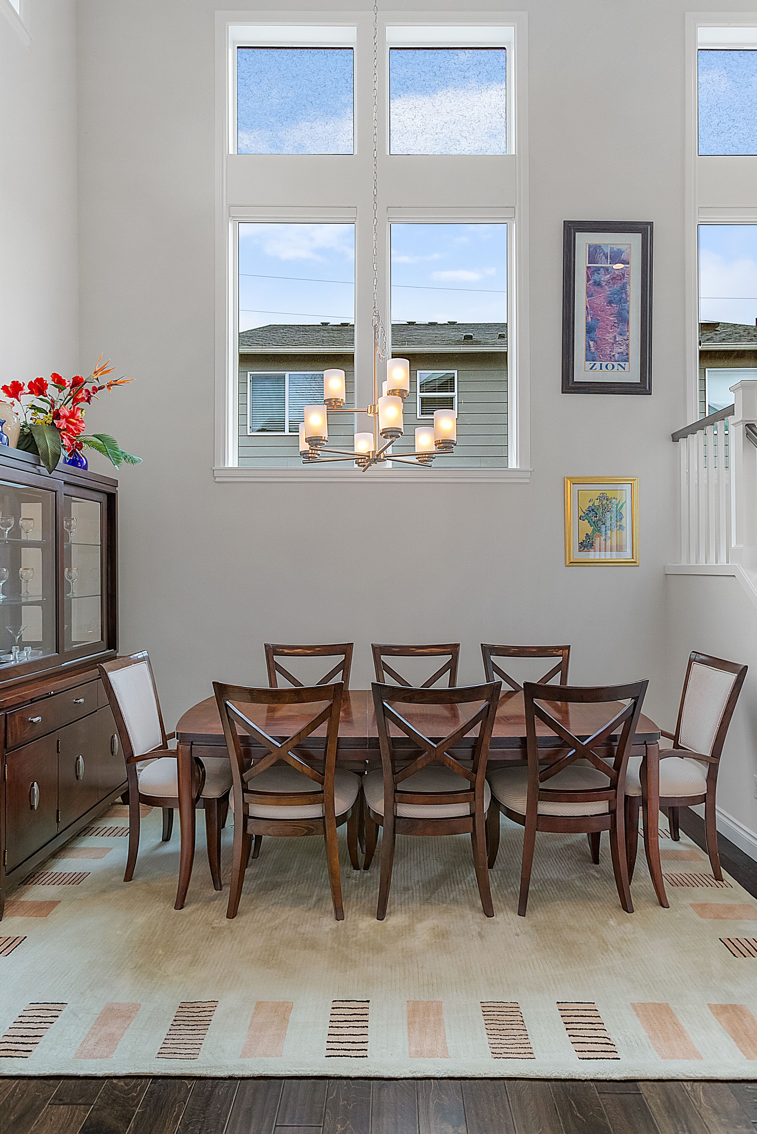 A dining area with a wooden table and chairs, a chandelier, and a view of the outdoors through large windows.