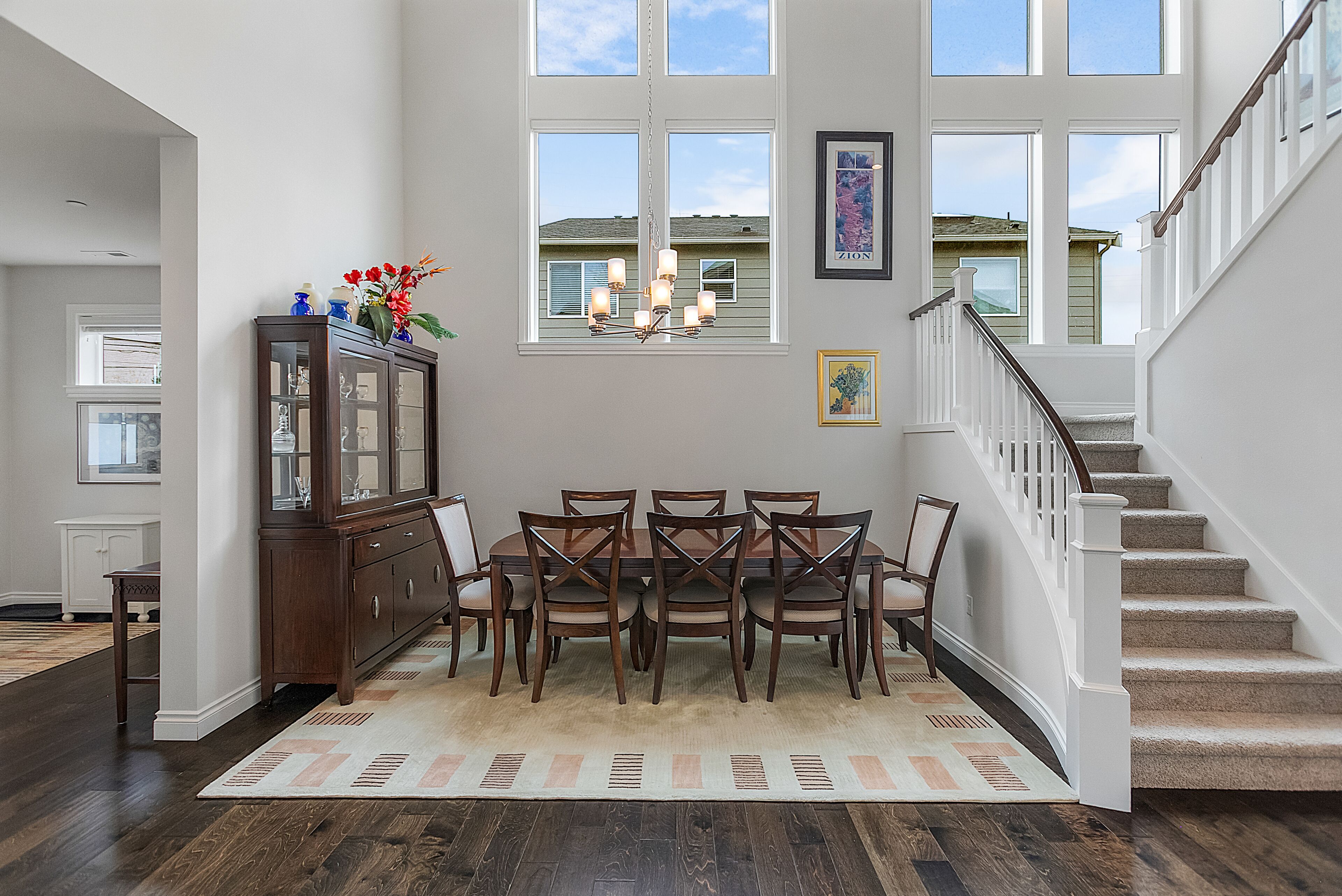 A dining area with a wooden table and chairs, a chandelier, and a view of the outside through large windows.
