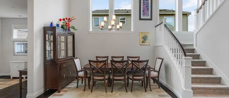 A dining area with a wooden table and chairs, a chandelier, and a view of the outside through large windows.