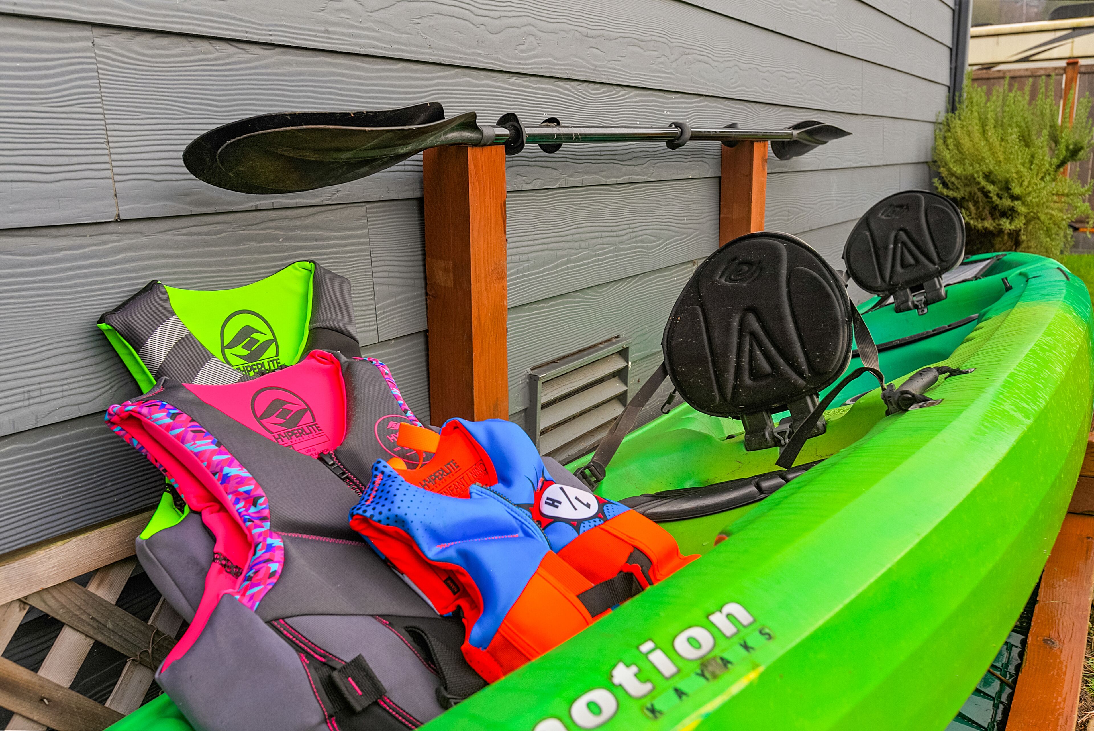A kayak with a green body and a paddle resting on a wooden post.