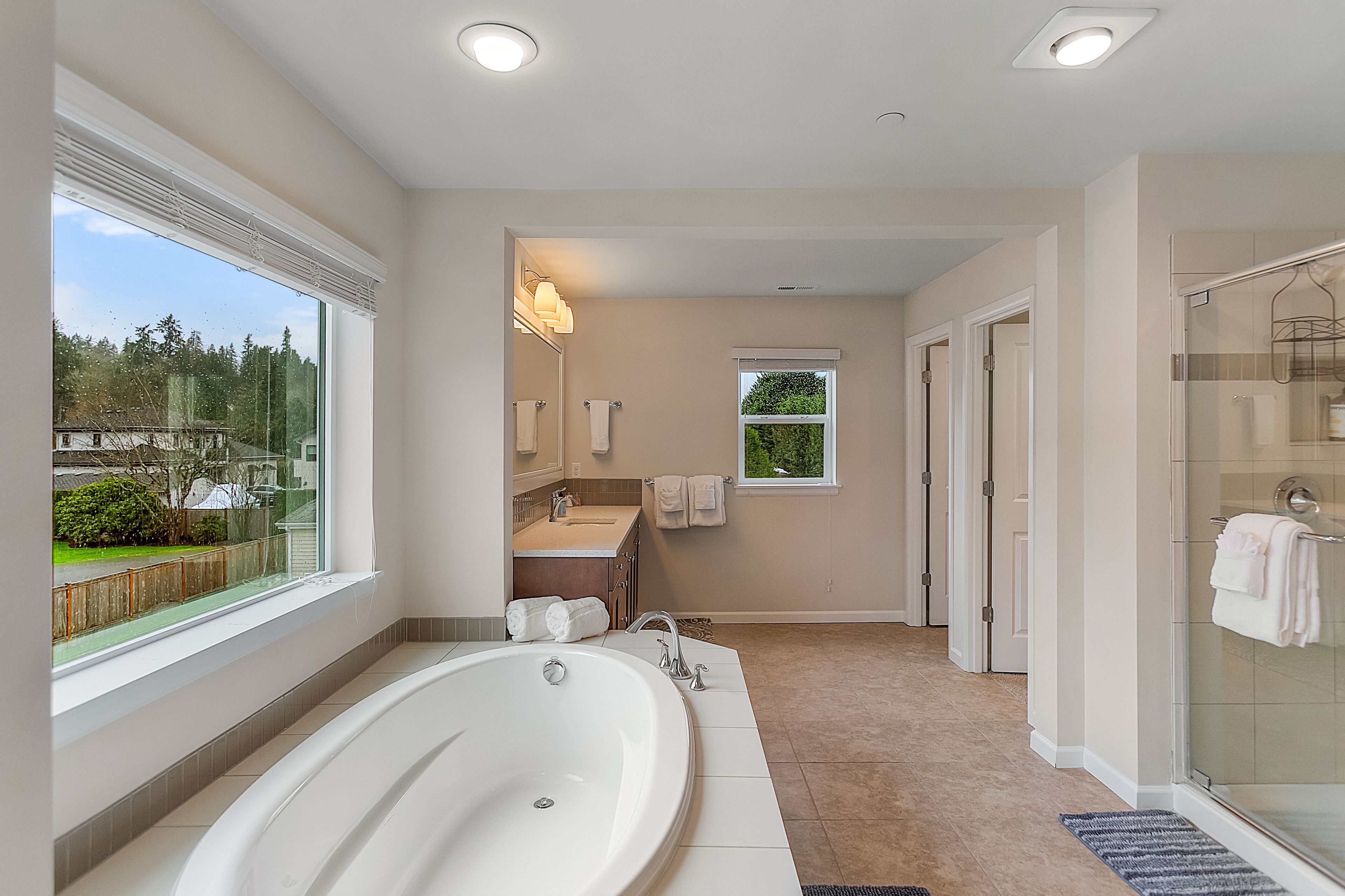 A modern bathroom with a large bathtub, a glass shower enclosure, and a view of the outdoors.