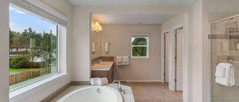 A modern bathroom with a large bathtub, a glass shower enclosure, and a view of the outdoors.