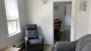 A living room with a grey sofa, a black leather chair, a wooden coffee table, and a wooden dining table with chairs. - Ocean view 2 bedroom apartment (Old Orchard Beach)