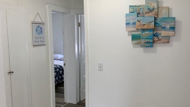 A hallway with wooden flooring, white walls, and a door leading to a bedroom. There is a wall-mounted artwork depicting beach scenes. - Ocean view 2 bedroom apartment (Old Orchard Beach)