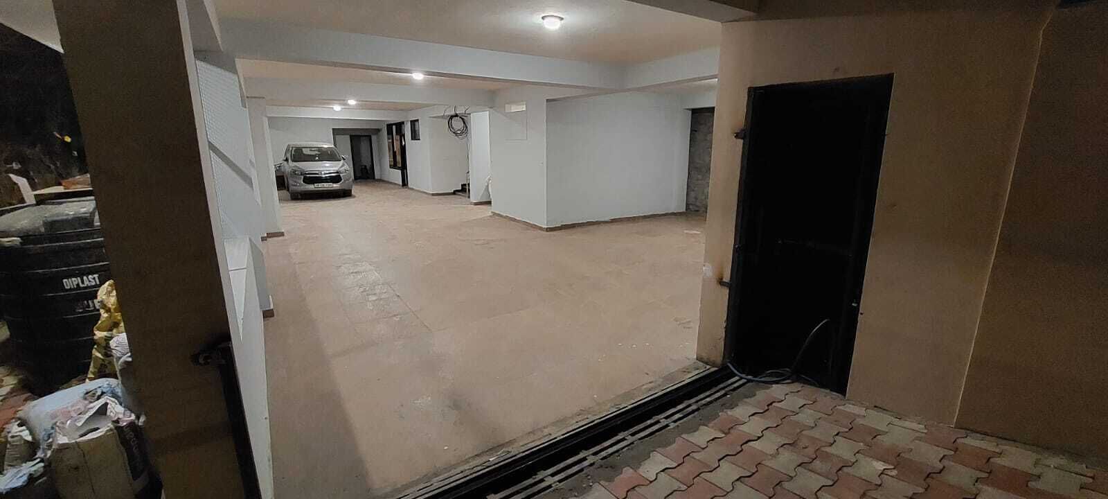 A hallway with a car parked in the distance, a black door on the right, and a vent on the floor.