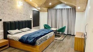 A modern bedroom with a wooden bed, green chairs, and a small wooden table. - Apple Woods (Manali)