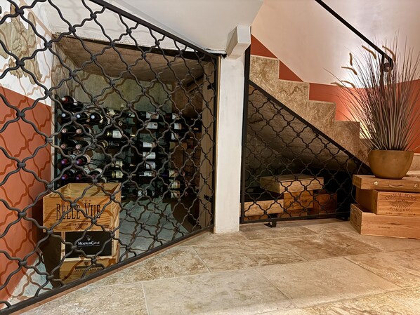 A wine cellar with wooden crates and bottles, a staircase with a geometric design, and a potted plant. - Pax & Amor - Boutique B&B (Mazerolles-du-Razès)