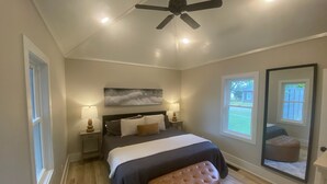 Quarto com cama, duas mesas de cabeceira, um ventilador de teto e uma janela grande.