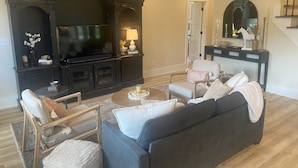 Uma sala de estar com um móvel de entretenimento escuro, uma televisão, um sofá e uma mesa de centro.
