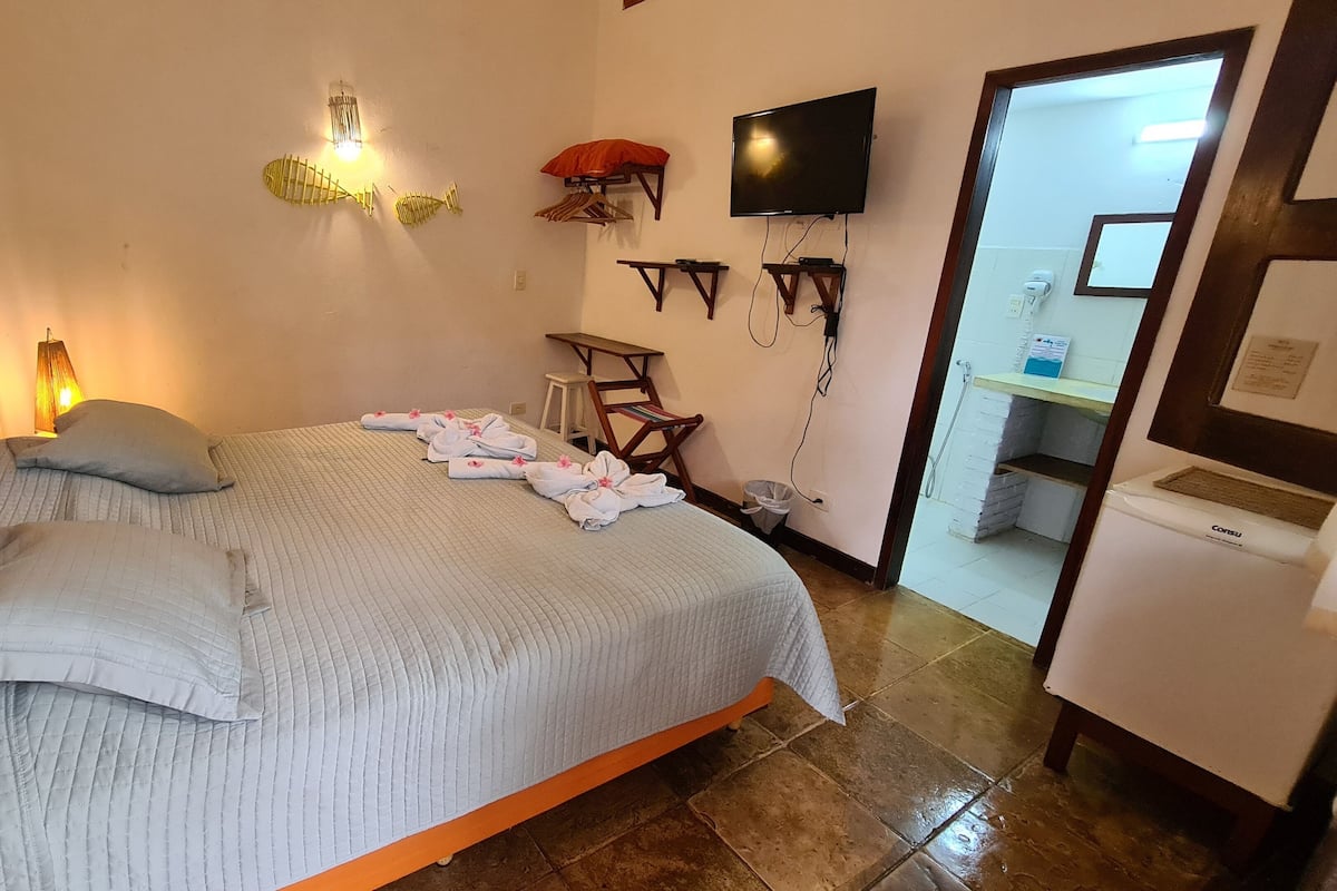 Habitación de hotel con cama, televisor montado en la pared, una mesita y un baño visible a través de una puerta abierta.