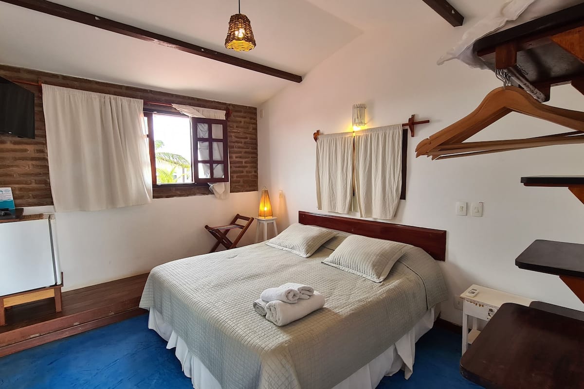 Un dormitorio con cama, escritorio, silla, lámpara colgante y una cruz en la pared.