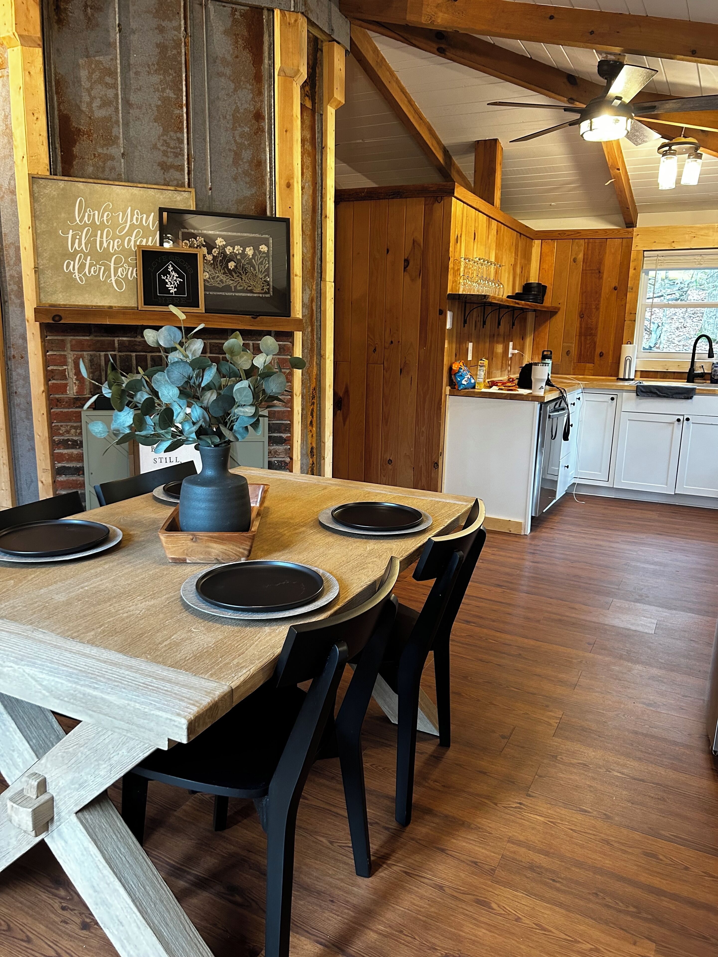 Un comedor rústico con una mesa de madera preparada para cuatro comensales, una pared de ladrillo y un ventilador de techo.