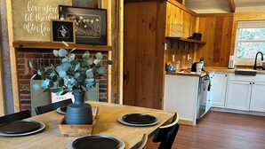 Un coin repas rustique avec une table en bois dressée pour quatre personnes, un mur en briques et un ventilateur de plafond.