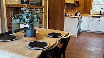 Un comedor rústico con una mesa de madera preparada para cuatro comensales, una pared de ladrillo y un ventilador de techo.