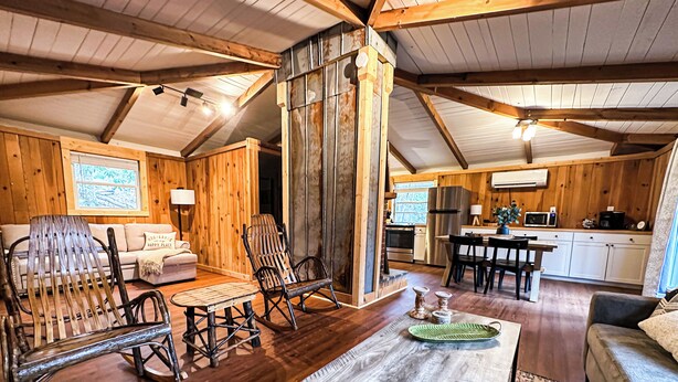 L’intérieur chaleureux d’un chalet avec des murs en bois, un salon doté d’un canapé, de fauteuils à bascule et d’une table basse, ainsi qu’un coin cuisine avec un réfrigérateur et un four à micro-ondes.