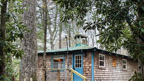 Une cabane rustique avec une façade en bois, une porte bleue et un petit porche doté d’une balustrade en bois.