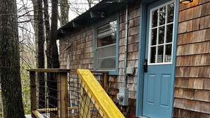 Une cabane en bois avec une porte bleue, un escalier en bois avec une rampe jaune et une balustrade en métal.