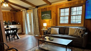 Un intérieur de chalet chaleureux avec une table à manger en bois, un canapé agrémenté de coussins à motifs, un coin café et un panneau indiquant « HIGHLANDS, altitude 4 400 ».