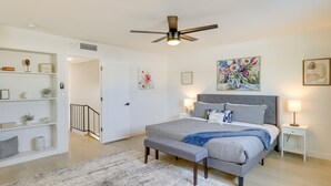 Ein Schlafzimmer mit einem Bett, Nachttischen, einem Deckenventilator und Kunstwerken an den Wänden.