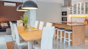 A modern kitchen with white cabinetry, a central island with stools, and pendant lighting. - Luxury Pool Villa Feliz (Dražin Vrt)