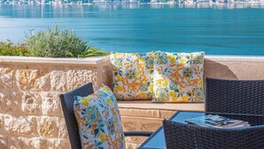 A terrace with wicker furniture, a stone wall, and a view of a lake and distant buildings. - Luxury Pool Villa Feliz (Dražin Vrt)