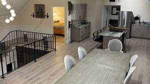Eine moderne Küche mit einer zentralen Kochinsel, ein Essbereich mit großem Tisch und Stühlen sowie eine Treppe zu einer oberen Ebene.