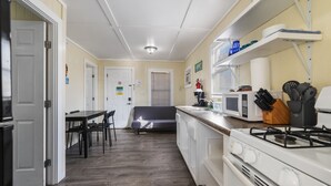 Une cuisine compacte avec des appareils électroménagers blancs, un coin repas avec une table et des chaises noires, et un petit coin salon avec un canapé.