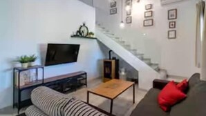 A modern living room with a sofa, a coffee table, a TV, and a staircase. - Casa Rural de Diseño (Alhaurín el Grande)