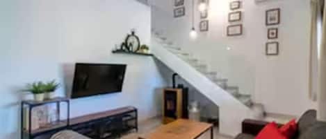 Un salon moderne avec un canapé, une table basse, un téléviseur et un escalier.