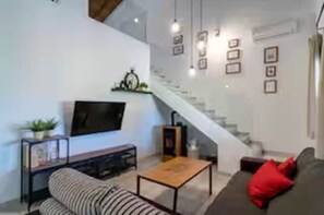 A modern living room with a sofa, a coffee table, a TV, and a staircase. - Casa Rural de Diseño (Alhaurín el Grande)