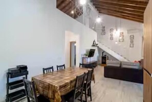 A dining area with a wooden table and chairs, a staircase, and a sofa. - Casa Rural de Diseño (Alhaurín el Grande)