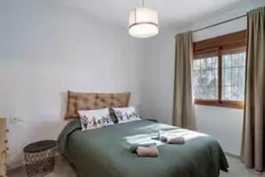 A bedroom with a bed, a bedside table, a lamp, and a window with curtains. - Casa Rural de Diseño (Alhaurín el Grande)