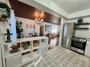 A modern kitchen with a built-in oven and refrigerator, wooden ceiling, and a dining area with chairs and a table.