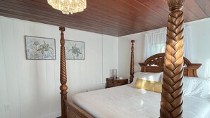 Ein Bett mit Baldachin, ein Holzkopf- und Fußteil, eine Chandelüster und zwei gerahmte Schildkrötenbilder an der Wand.