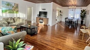 Ein geräumiges Wohnzimmer mit Holzboden, einer Couch, einem Couchtisch und einem Essbereich mit Stühlen und einem Tisch.