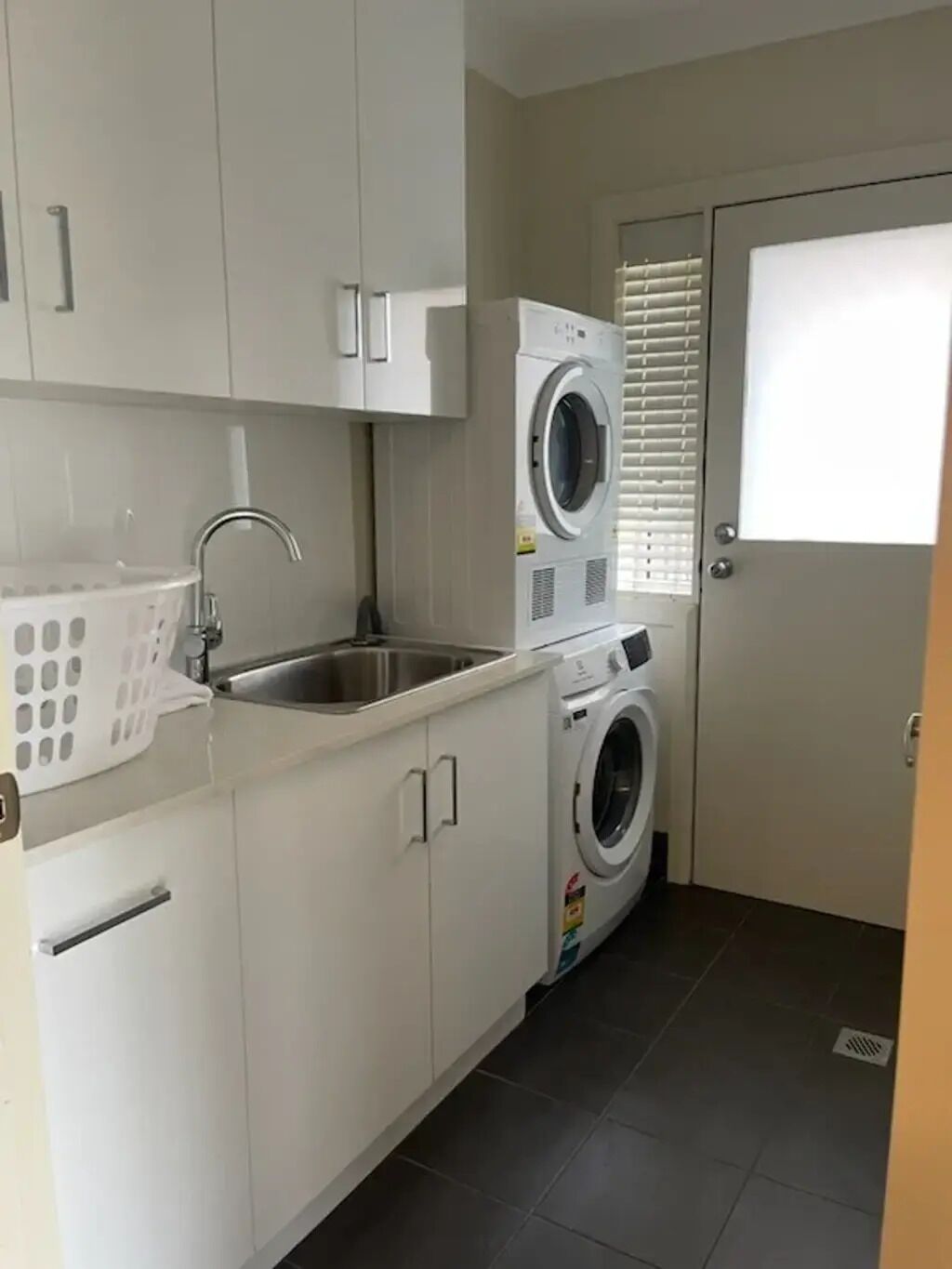 A compact laundry room with a washing machine, a sink, and a drying rack.