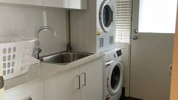 A compact laundry room with a washing machine, a sink, and a drying rack.